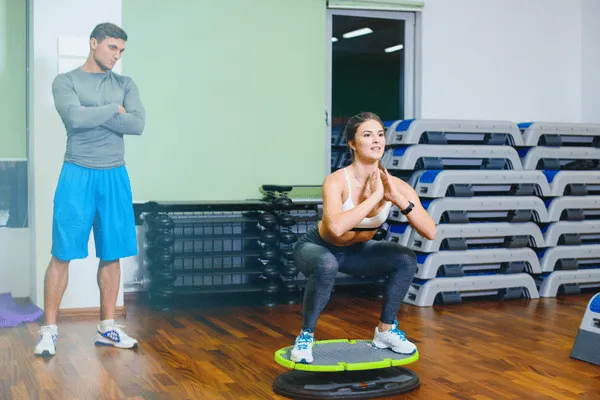 Trainer watches woman squat on balance disc during Performance Rehab session